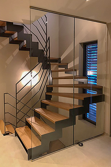 halbgewendelte Treppe mit ausgelaserten Treppenwangen in abgetreppter Form, Stufen aus Eiche Holz, modernem Geländer aus Flacheisen und einem raumhohen Glaselement/Glaswand