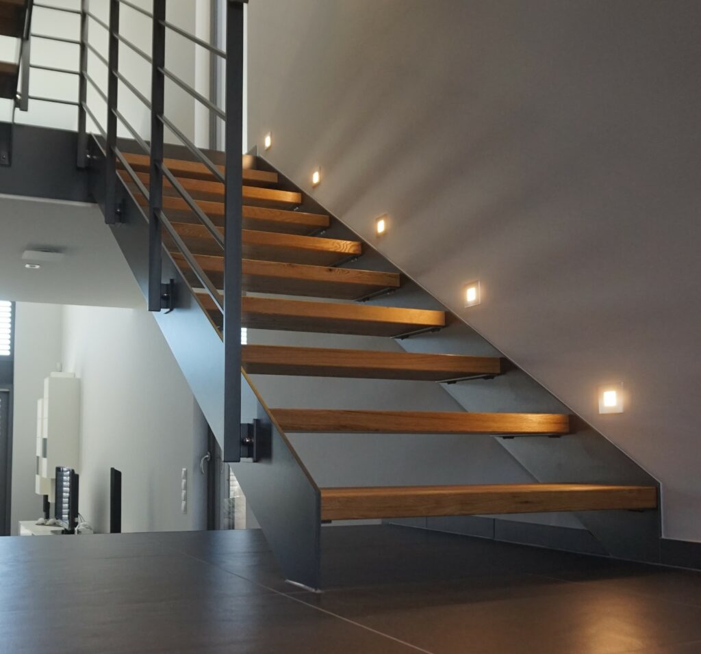 Moderne, maßgefertigte Stahl-Holz-Treppe mit Massivholzstufen und integrierter Beleuchtung, realisiert von metallic DESIGN Sàrl – hochwertiger Metallbau aus Luxemburg für exklusive Design-Innentreppen