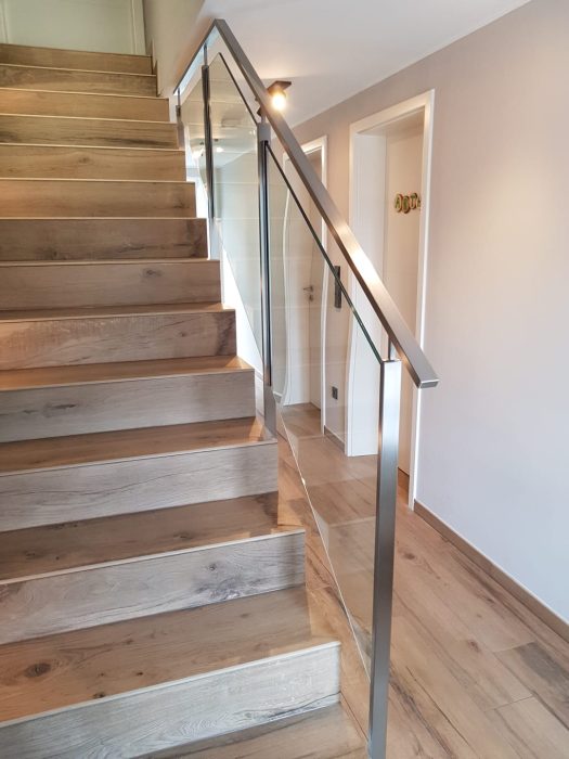 Moderne Innentreppe mit massiven Holzstufen und Glasgeländer mit Edelstahl-Handlauf, maßgefertigt von metallic DESIGN Sàrl – hochwertiger Metallbau aus Luxemburg