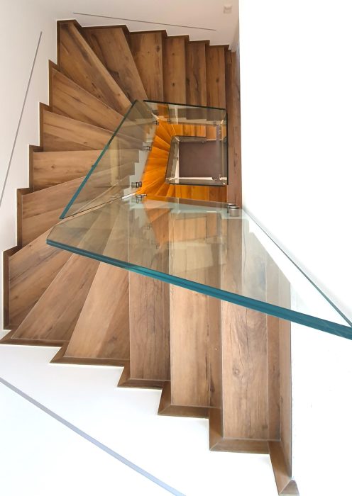 Moderne, gewendelte Innentreppe aus Stahl mit massiven Holzstufen und Glasgeländer, maßgefertigt von metallic DESIGN Sàrl – exklusiver Metallbau aus Luxemburg